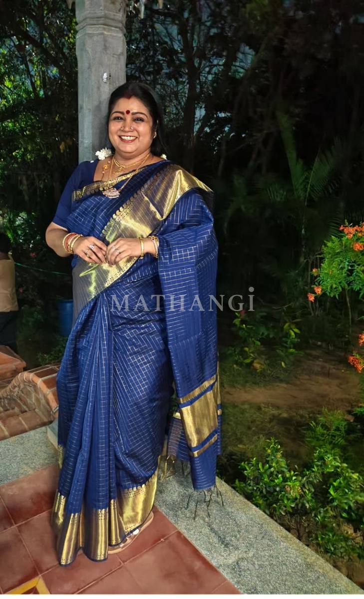 A navy blue saree with fine gold checks and a broad gold zari border, worn in a garden after dark
